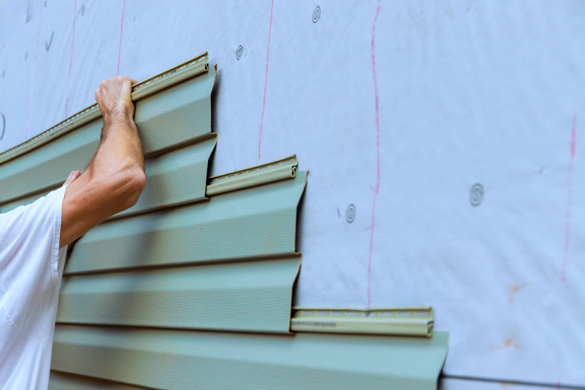 Construction worker carefully places installing new pvc vinyl siding siding panels on building exterior wall, Maple Grove